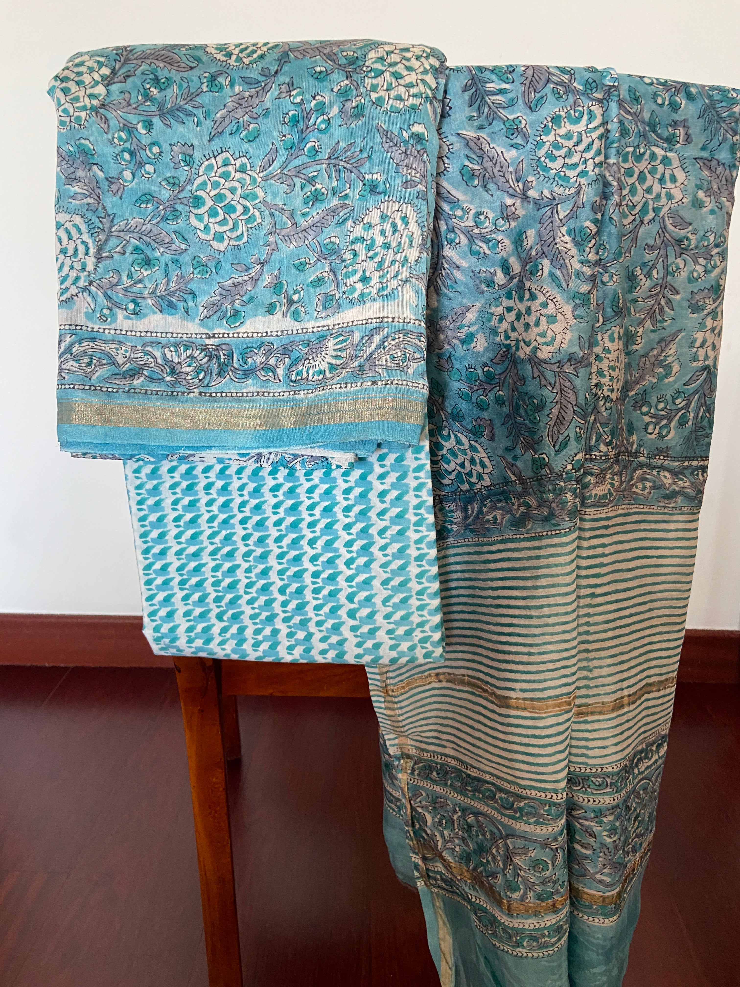 Peacock blue Chanderi handloom 3-piece suit draped on chair - kurta with padded geometric motifs in cream and gold, striped dupatta with teal and gold borders - unstitched from Chanderi, Madhya Pradesh | Bloomton Designs