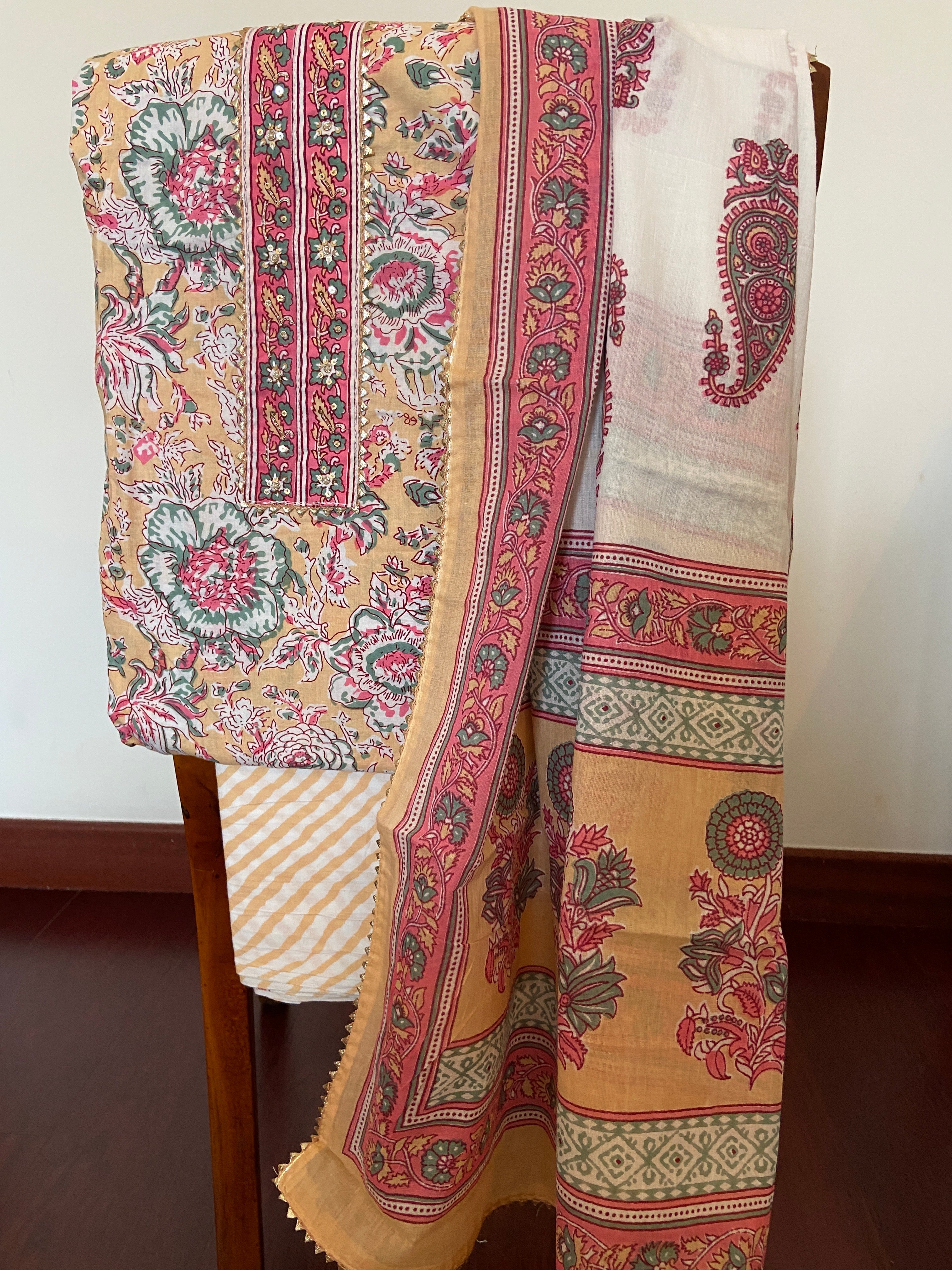 Cotton Gota Patti 3-piece suit draped on chair - cream kurta with vibrant hand-block printed paisley motifs, pink dupatta with gold gota border and gota neckline detailing - festive Rajasthani traditional wear | Bloomton Designs